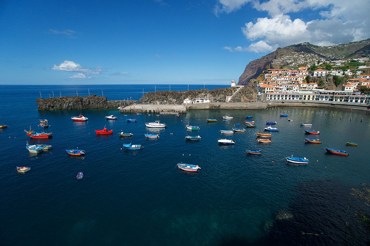Blauer Hafen auf Madeira mit kleinen farbigen Booten und Küstenort